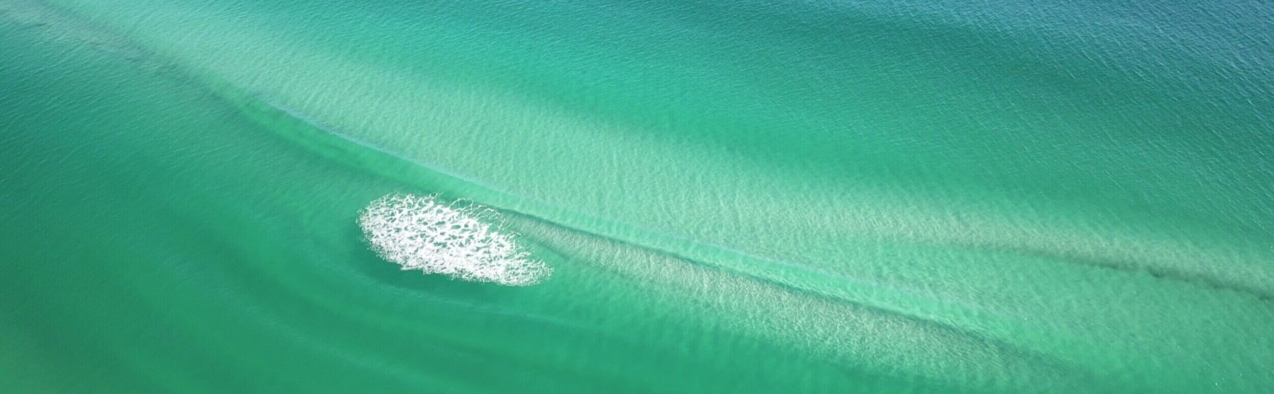 A soft wave rolling toward the shore over the emerald green Gulf of Mexico along 30A